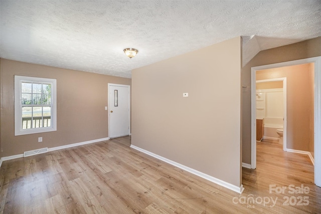 empty room with visible vents, baseboards, light wood-style floors, and a textured ceiling