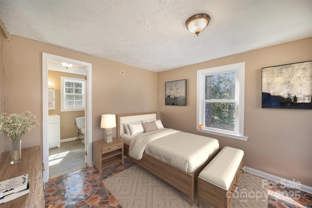 bedroom with ensuite bath, stone finish floor, baseboards, and a textured ceiling