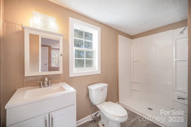 full bath with toilet, vanity, a stall shower, a textured ceiling, and tile walls