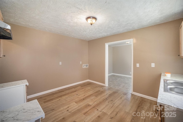 interior space with light wood finished floors, baseboards, light countertops, a textured ceiling, and a sink