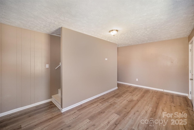 empty room with light wood finished floors, a textured ceiling, stairs, and baseboards