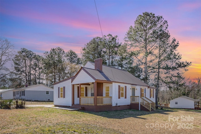 view of front of property featuring a porch, a front yard, a chimney, metal roof, and crawl space