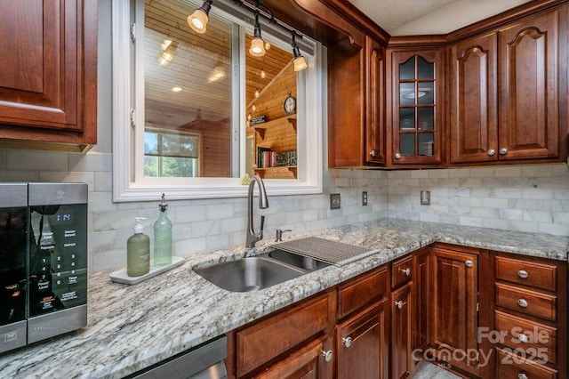 kitchen featuring tasteful backsplash, stainless steel microwave, glass insert cabinets, light stone counters, and a sink