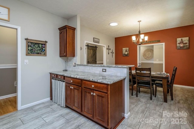 kitchen with baseboards, a peninsula, a chandelier, and light stone countertops