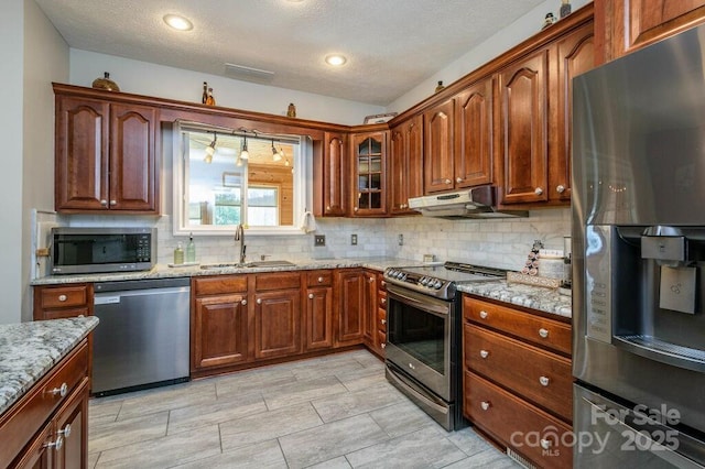 kitchen featuring under cabinet range hood, stainless steel appliances, light stone countertops, and a sink