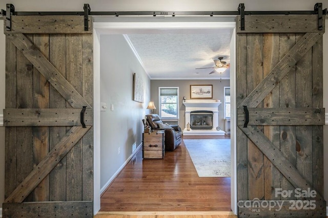 corridor featuring ornamental molding, a textured ceiling, a barn door, and wood finished floors