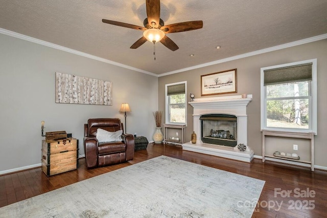 living area with crown molding, a ceiling fan, wood-type flooring, and a fireplace with raised hearth