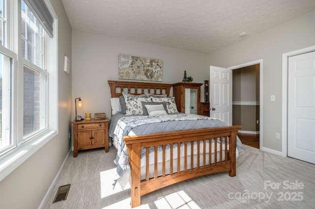 bedroom featuring light carpet, visible vents, a textured ceiling, and baseboards