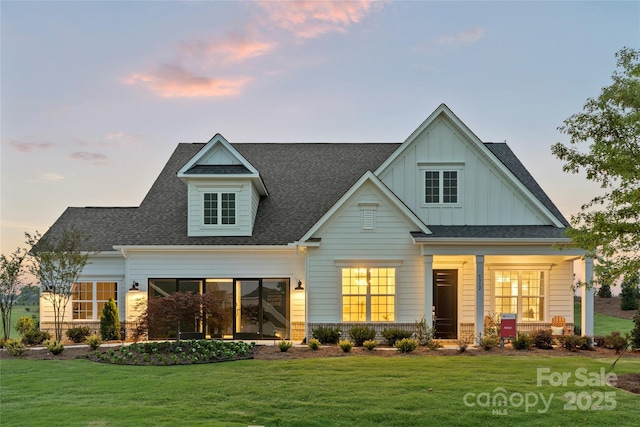 back of property at dusk featuring a porch, a yard, board and batten siding, and roof with shingles