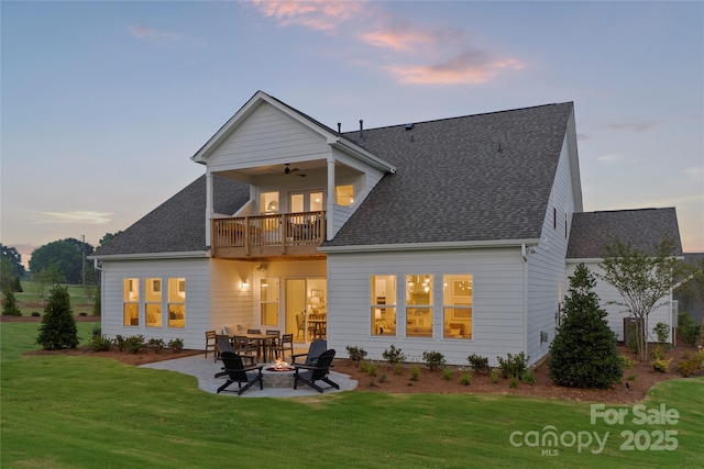 back of house at dusk with a patio, a balcony, a fire pit, and a lawn