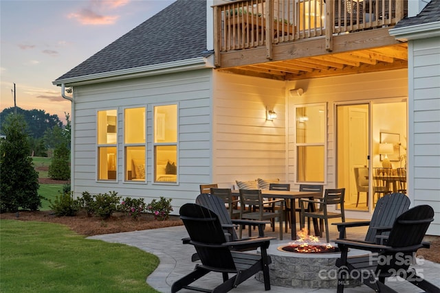 patio terrace at dusk featuring a balcony, outdoor dining space, and an outdoor fire pit