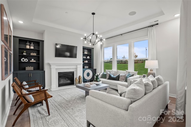 living room featuring visible vents, built in features, a tray ceiling, wood finished floors, and a premium fireplace