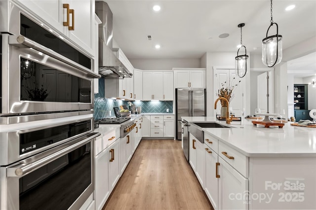 kitchen with decorative backsplash, stainless steel appliances, wall chimney exhaust hood, and light countertops