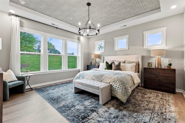 bedroom with a raised ceiling, a notable chandelier, light wood-style flooring, recessed lighting, and baseboards