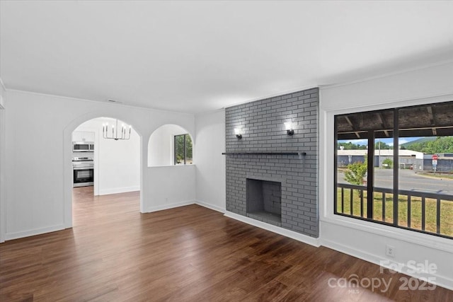 unfurnished living room with wood finished floors, visible vents, baseboards, arched walkways, and a brick fireplace