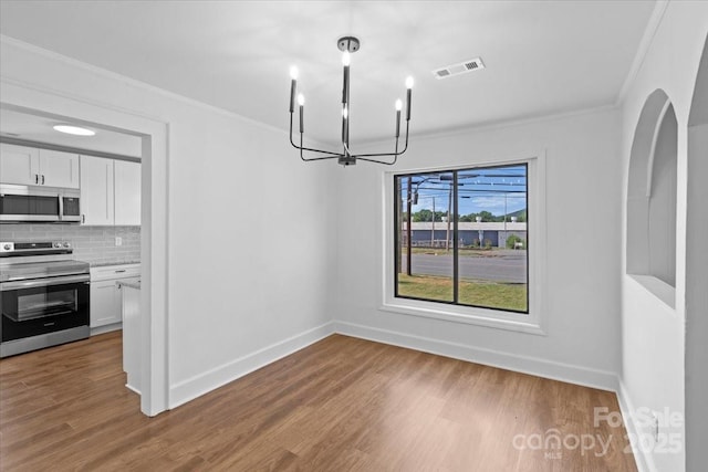 unfurnished dining area with wood finished floors, baseboards, visible vents, ornamental molding, and a notable chandelier