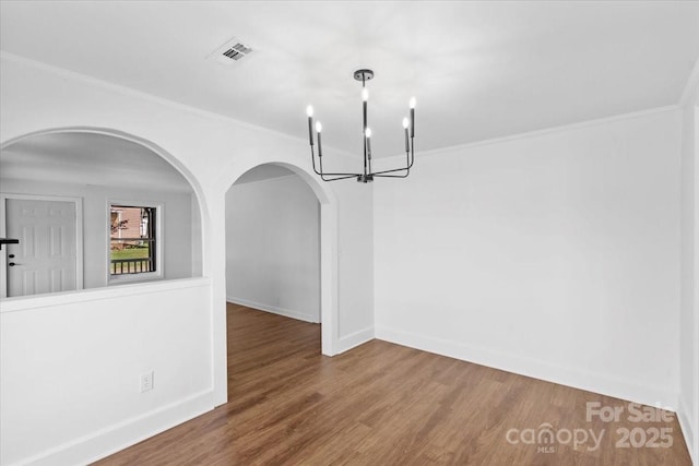 unfurnished dining area featuring visible vents, crown molding, an inviting chandelier, and wood finished floors