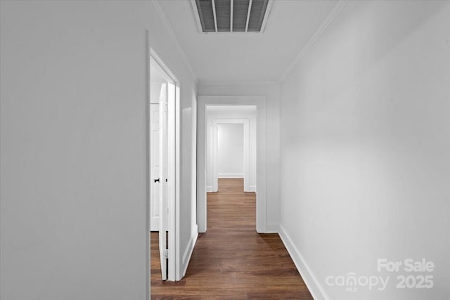 hallway with visible vents, baseboards, ornamental molding, and dark wood finished floors