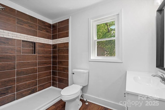 full bathroom featuring vanity, wood finished floors, baseboards, a tile shower, and toilet