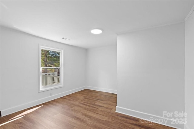 unfurnished room with visible vents, baseboards, wood finished floors, and ornamental molding