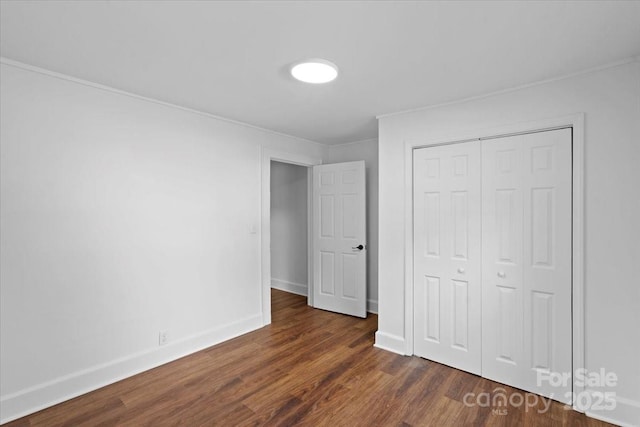 unfurnished bedroom featuring a closet, dark wood-type flooring, baseboards, and ornamental molding