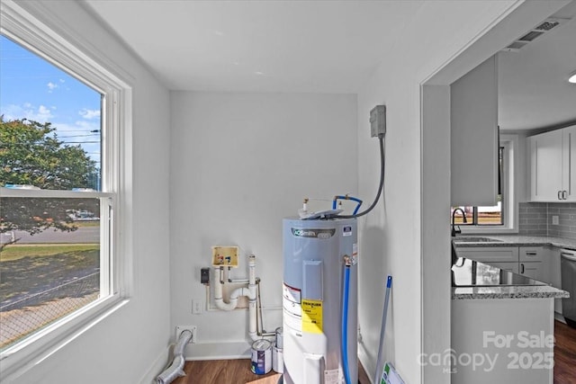 utility room with water heater, visible vents, and a sink