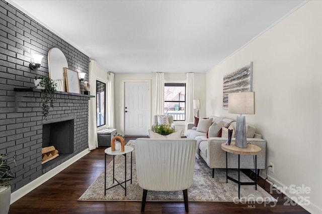 living room with a brick fireplace, crown molding, baseboards, and wood finished floors