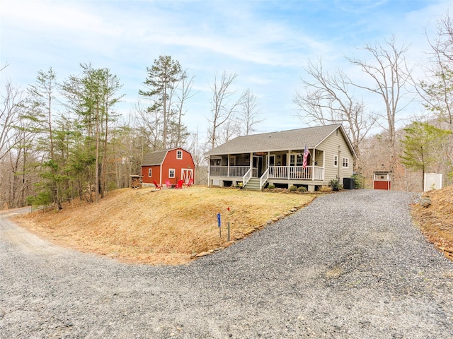 view of front of home featuring an outbuilding, cooling unit, covered porch, gravel driveway, and a front yard