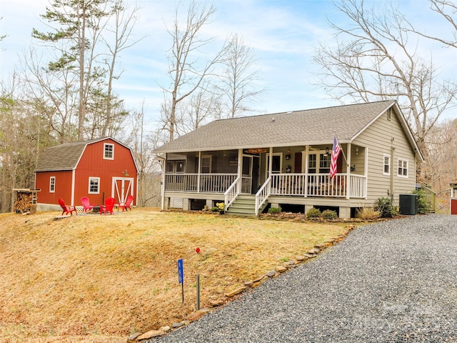 view of front facade with central air condition unit, an outbuilding, a fire pit, a front yard, and a shingled roof