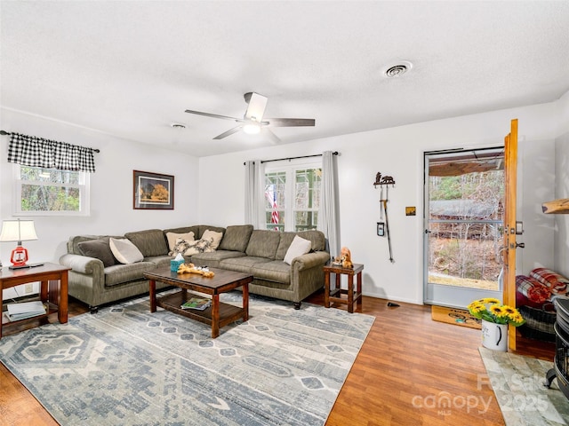 living room featuring visible vents, baseboards, wood finished floors, a textured ceiling, and a ceiling fan