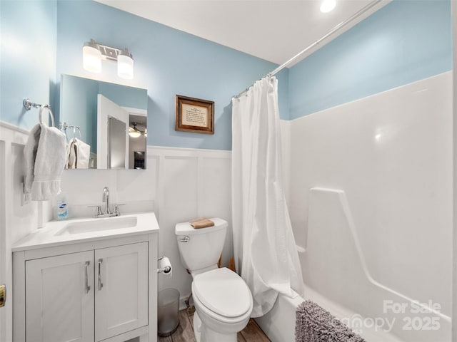 full bath featuring a wainscoted wall, toilet, shower / bath combo, a decorative wall, and vanity