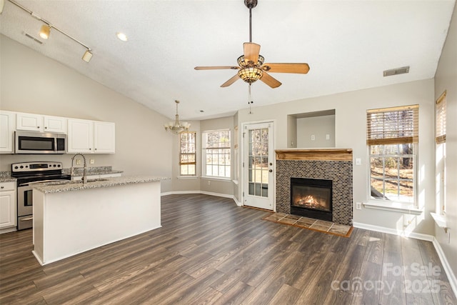 kitchen featuring open floor plan, light stone counters, a fireplace, stainless steel appliances, and white cabinetry