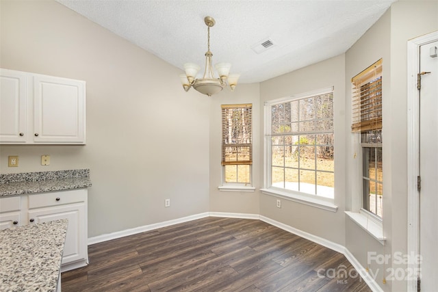 unfurnished dining area with visible vents, baseboards, dark wood-style flooring, a textured ceiling, and a notable chandelier