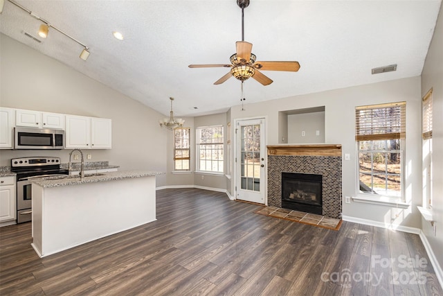 kitchen with light stone countertops, dark wood finished floors, open floor plan, appliances with stainless steel finishes, and white cabinets