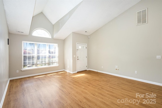 unfurnished living room with visible vents, light wood-style flooring, high vaulted ceiling, and baseboards