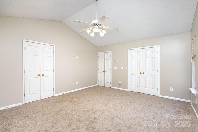 unfurnished bedroom featuring a ceiling fan, carpet, baseboards, lofted ceiling, and two closets