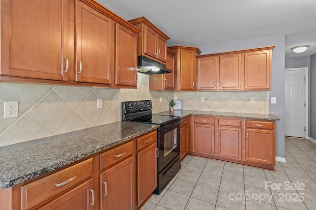 kitchen featuring under cabinet range hood, brown cabinetry, dark stone countertops, and black range with electric stovetop