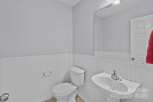 bathroom with wainscoting, toilet, and a sink