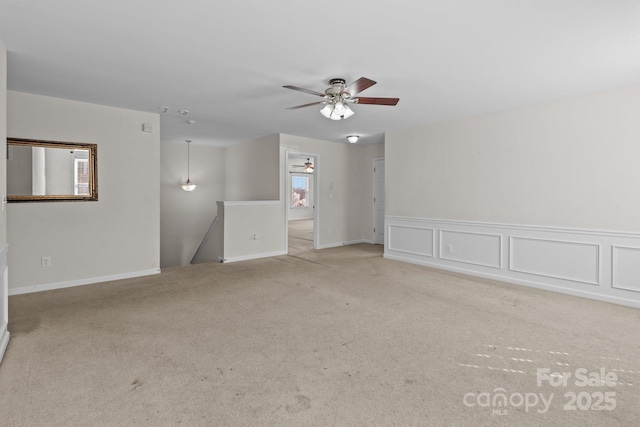 carpeted empty room featuring ceiling fan and a decorative wall