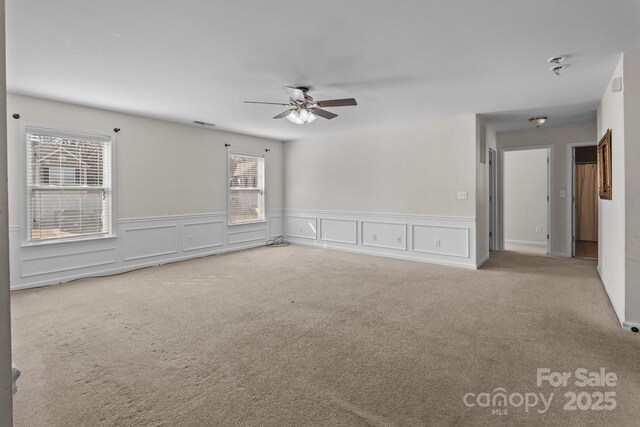 empty room with a wainscoted wall, ceiling fan, and carpet flooring