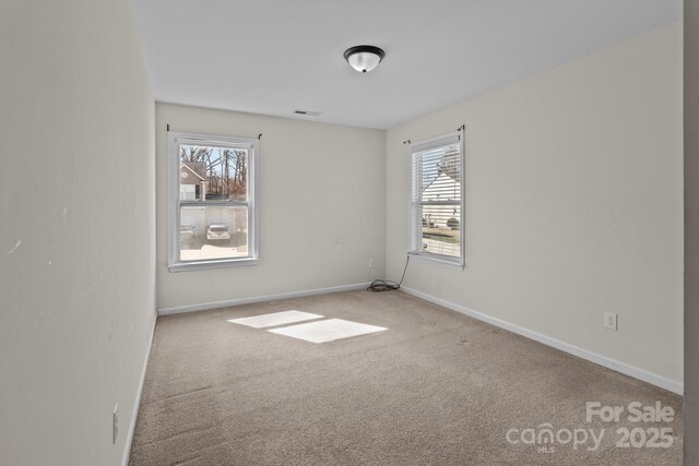 carpeted spare room featuring a wealth of natural light, visible vents, and baseboards