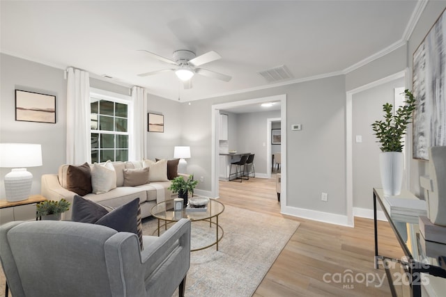 living room with visible vents, baseboards, ceiling fan, light wood-type flooring, and ornamental molding