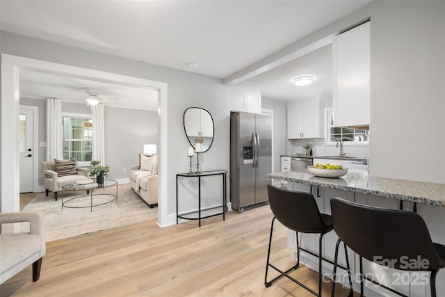 kitchen featuring light stone counters, stainless steel appliances, white cabinetry, light wood-type flooring, and backsplash