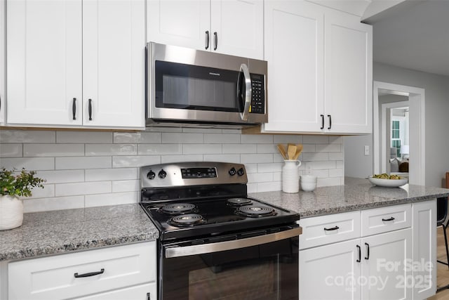 kitchen with stainless steel microwave, backsplash, electric range oven, and white cabinetry