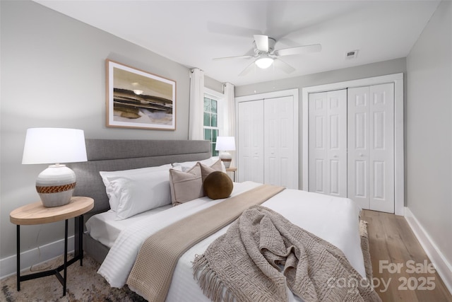 bedroom featuring visible vents, ceiling fan, baseboards, multiple closets, and wood finished floors