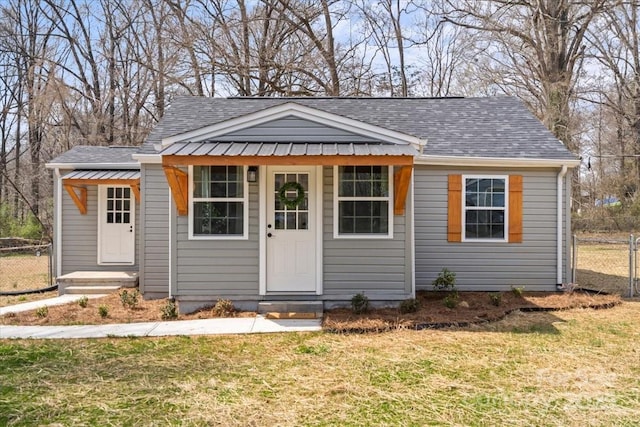 view of front facade with a front lawn, fence, and a shingled roof