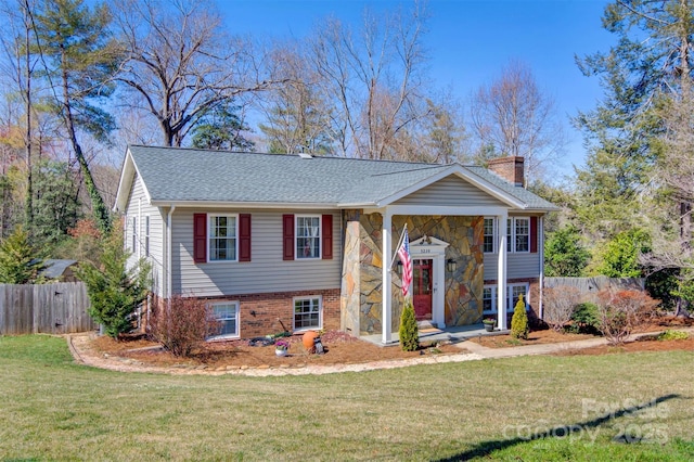 bi-level home featuring brick siding, a shingled roof, a front lawn, fence, and a chimney