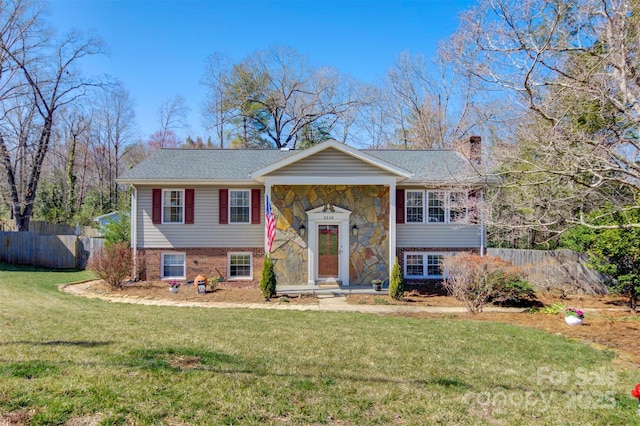 bi-level home featuring brick siding, a front lawn, fence, a chimney, and stone siding