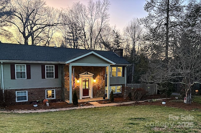 raised ranch with brick siding, a lawn, and a chimney