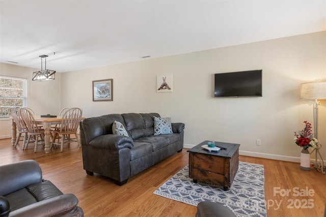 living area featuring baseboards, light wood-style floors, and a chandelier